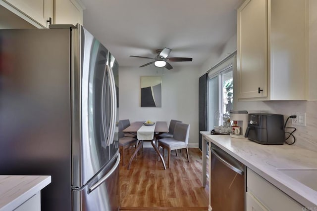 kitchen with appliances with stainless steel finishes, light wood-style floors, light stone counters, and ceiling fan