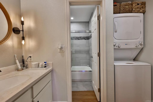 bathroom with shower / bathing tub combination, stacked washing maching and dryer, wood finished floors, and vanity