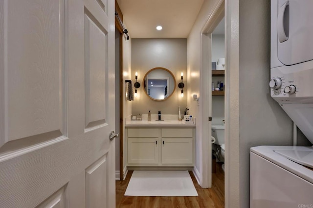 laundry room featuring a barn door, laundry area, a sink, wood finished floors, and stacked washer and clothes dryer