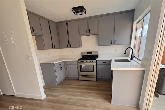 kitchen featuring stainless steel gas range oven, a sink, light wood-style floors, light countertops, and gray cabinets