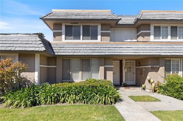 view of front facade with mansard roof, board and batten siding, and stucco siding