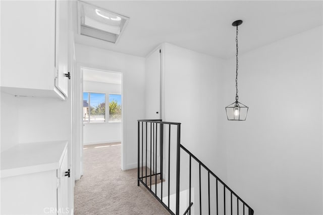 corridor featuring attic access, baseboards, light colored carpet, and an upstairs landing