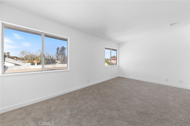 empty room with carpet, a textured ceiling, and baseboards