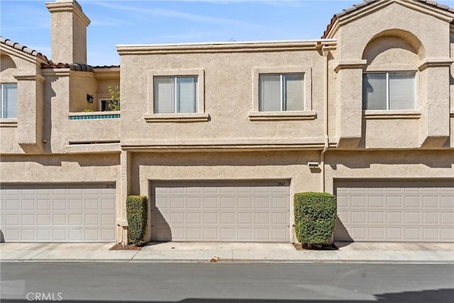 view of property featuring a garage, a tiled roof, and stucco siding