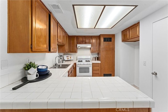 kitchen featuring brown cabinets, visible vents, white range with gas cooktop, a sink, and under cabinet range hood