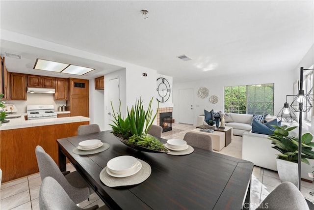 dining space featuring light tile patterned floors, a brick fireplace, and visible vents