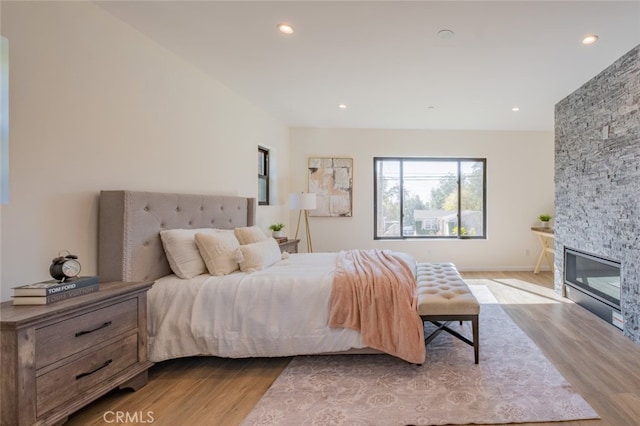 bedroom with baseboards, a stone fireplace, wood finished floors, and recessed lighting
