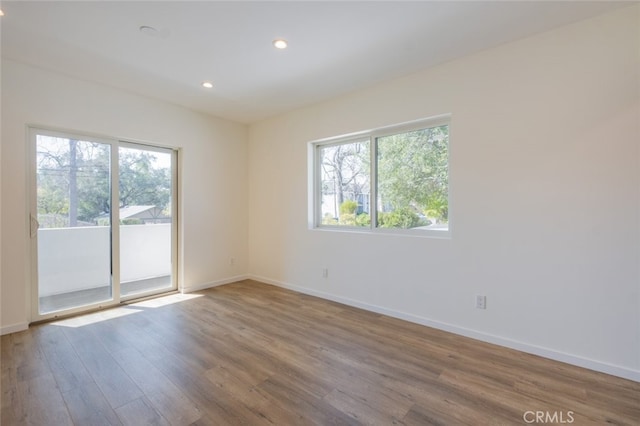 spare room featuring recessed lighting, a healthy amount of sunlight, baseboards, and wood finished floors