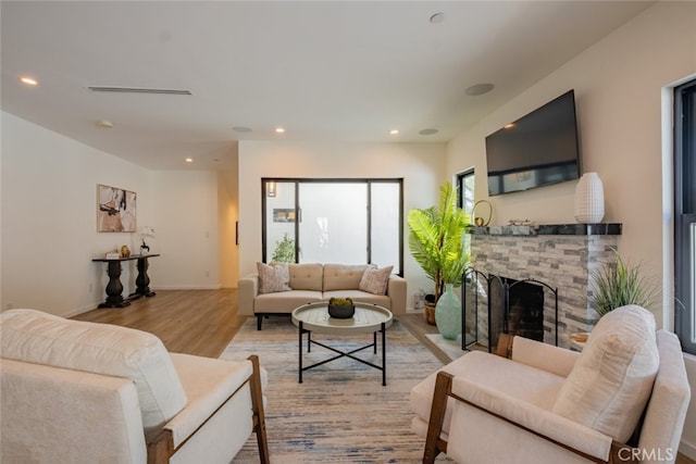 living room with visible vents, baseboards, a stone fireplace, light wood-style floors, and recessed lighting
