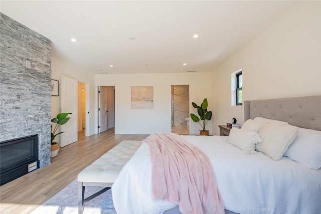 bedroom featuring a stone fireplace, wood finished floors, and recessed lighting