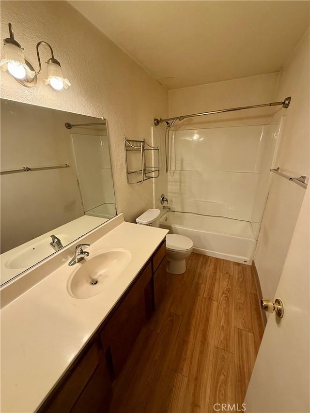 full bathroom featuring a textured wall, toilet, wood finished floors, vanity, and tub / shower combination