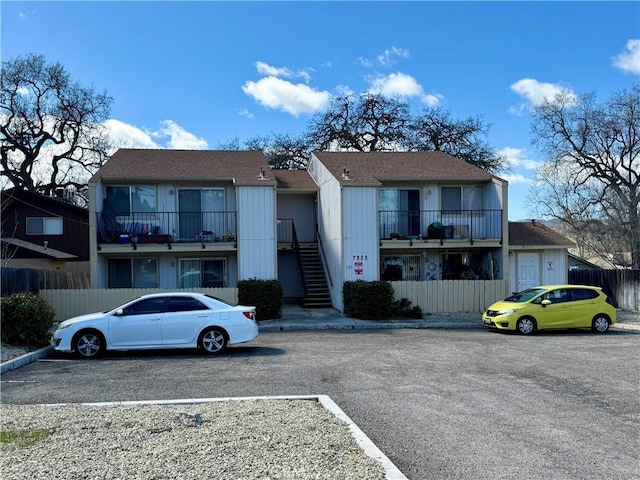 view of building exterior featuring stairs, fence, and uncovered parking