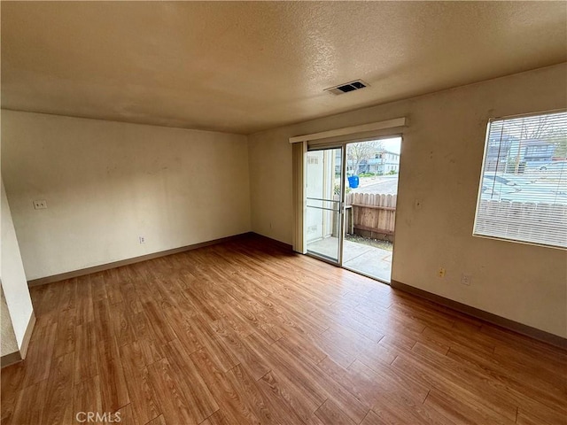 unfurnished room featuring visible vents, a textured ceiling, baseboards, and wood finished floors