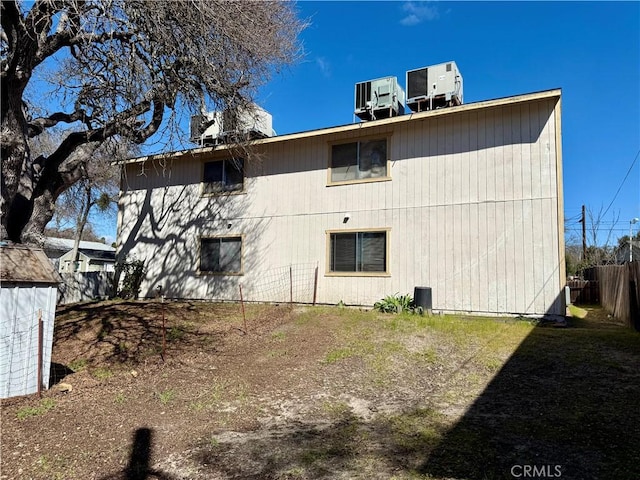 rear view of house with central AC unit, an outdoor structure, and fence