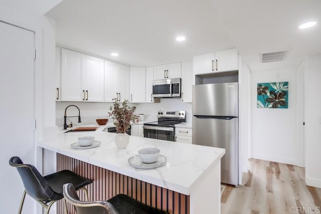 kitchen with a peninsula, a breakfast bar, a sink, visible vents, and appliances with stainless steel finishes