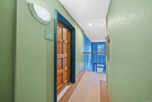 hallway with a textured wall, carpet flooring, and baseboards