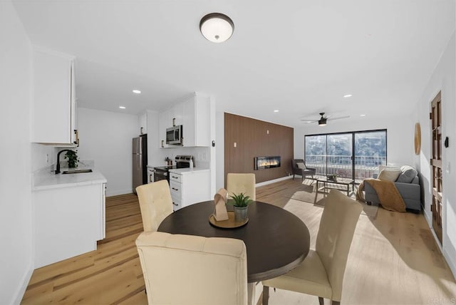 dining area with ceiling fan, recessed lighting, baseboards, light wood-type flooring, and a glass covered fireplace