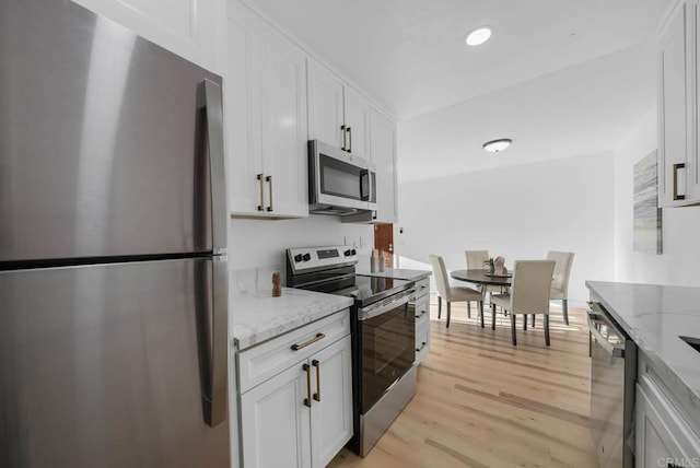 kitchen featuring recessed lighting, white cabinetry, appliances with stainless steel finishes, light stone countertops, and light wood finished floors