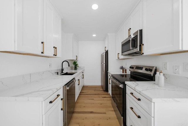 kitchen with appliances with stainless steel finishes, white cabinetry, a sink, and light wood-style flooring