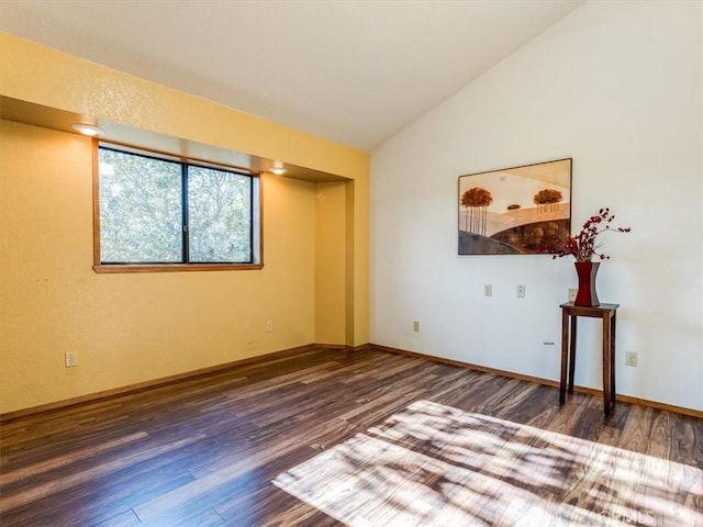 spare room featuring lofted ceiling, baseboards, and wood finished floors