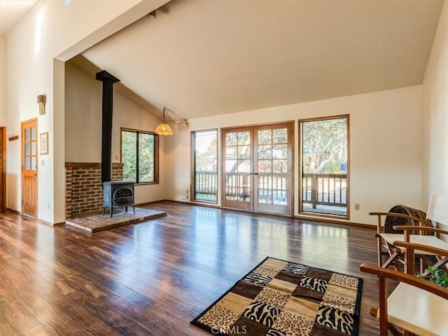 living room featuring high vaulted ceiling, wood finished floors, a wood stove, and baseboards