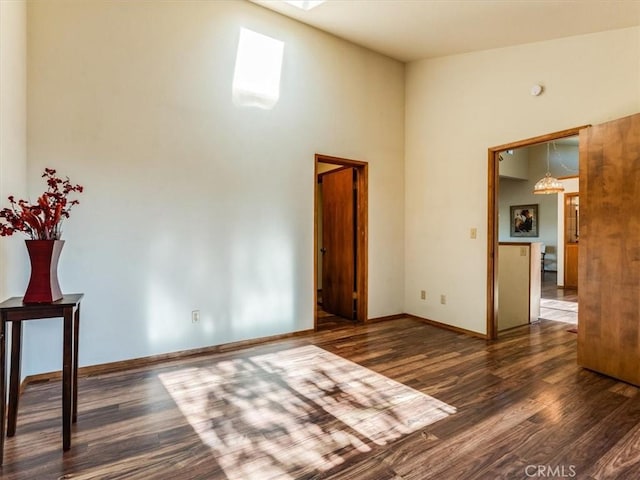 unfurnished room with a towering ceiling, baseboards, and wood finished floors