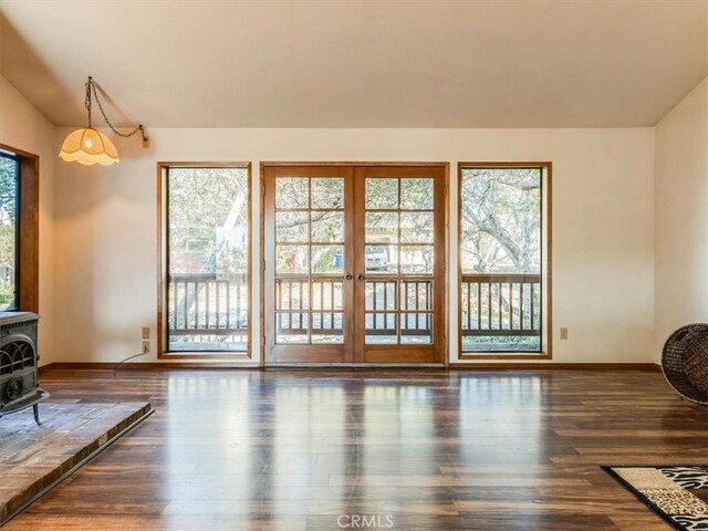 doorway with baseboards, wood finished floors, a wood stove, vaulted ceiling, and french doors