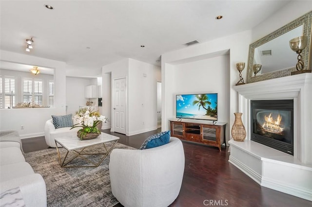 living room featuring baseboards, visible vents, wood finished floors, and a glass covered fireplace