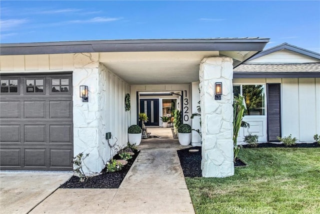 doorway to property with a garage, stone siding, and a yard