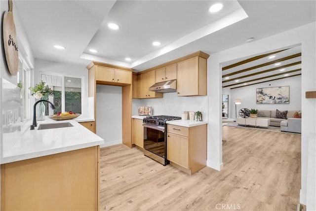 kitchen with stainless steel gas range oven, light brown cabinets, under cabinet range hood, a sink, and light wood-style floors