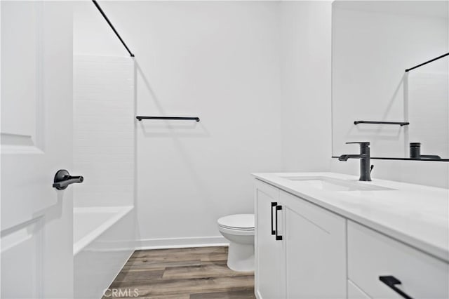 bathroom with toilet, wood finished floors, vanity, baseboards, and shower / bathing tub combination