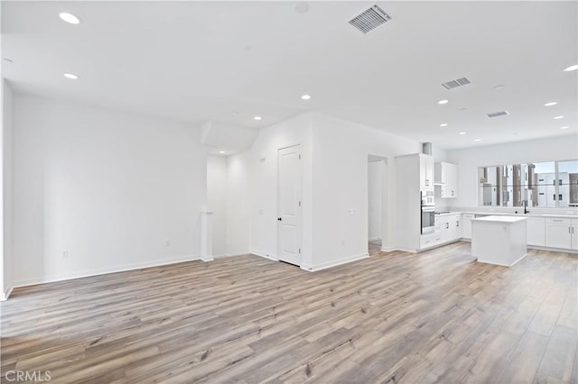 unfurnished living room featuring recessed lighting, a sink, visible vents, baseboards, and light wood-type flooring