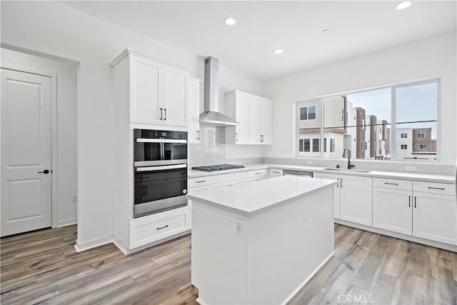 kitchen featuring recessed lighting, stainless steel double oven, a sink, wall chimney range hood, and black gas stovetop