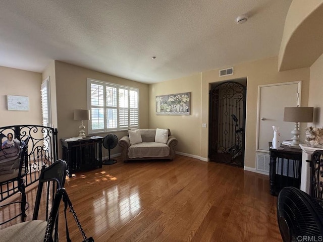 living room with a textured ceiling, wood finished floors, visible vents, and baseboards