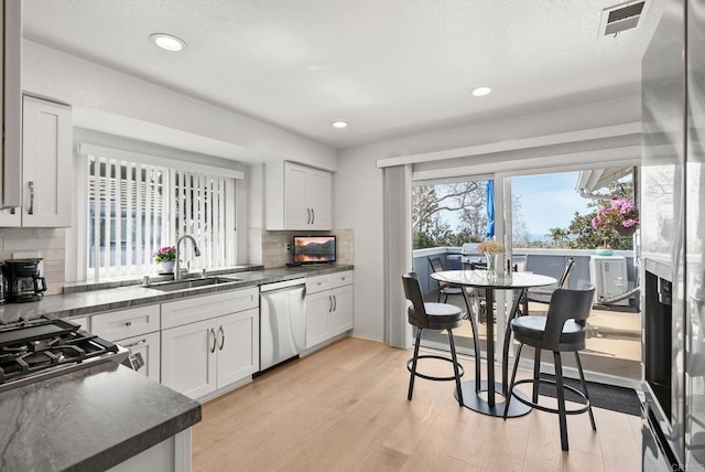 kitchen featuring visible vents, dark countertops, light wood-style flooring, a sink, and stainless steel dishwasher