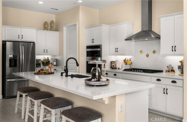 kitchen featuring white cabinets, stainless steel appliances, wall chimney range hood, and a sink