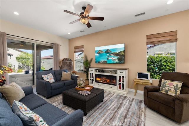 living room featuring a glass covered fireplace, visible vents, and ceiling fan