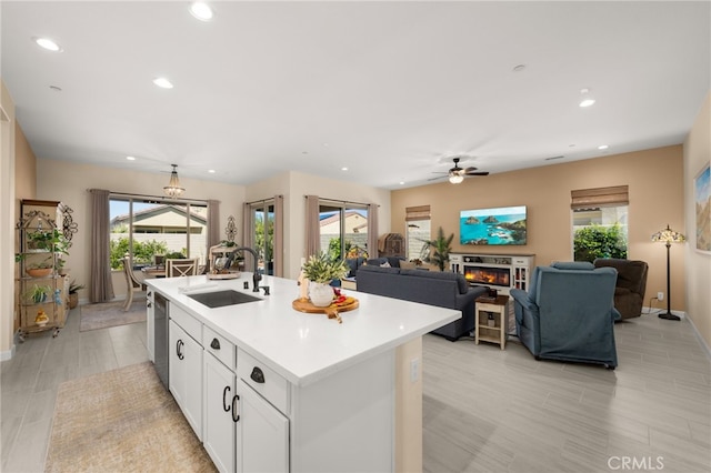 kitchen with a sink, stainless steel dishwasher, a glass covered fireplace, white cabinets, and light countertops