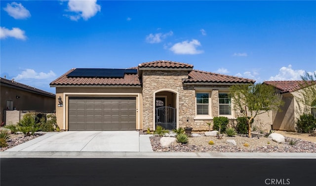 mediterranean / spanish home with a tiled roof, an attached garage, driveway, and roof mounted solar panels