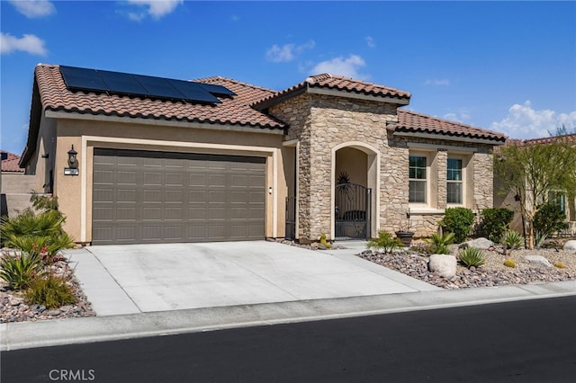 mediterranean / spanish house with concrete driveway, roof mounted solar panels, stucco siding, an attached garage, and a gate