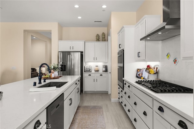 kitchen featuring white cabinets, wall chimney exhaust hood, appliances with stainless steel finishes, and a sink