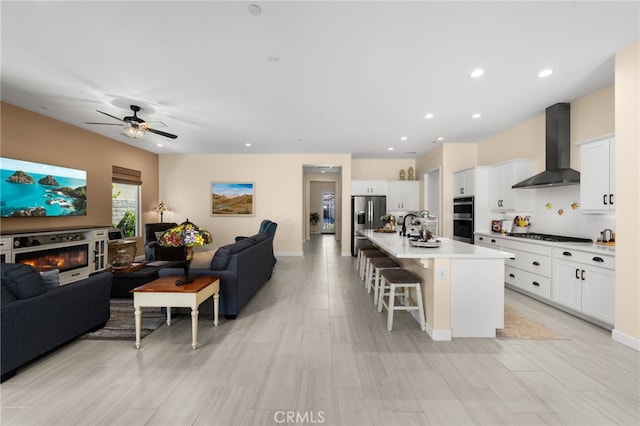 kitchen featuring a glass covered fireplace, a breakfast bar area, open floor plan, and wall chimney range hood