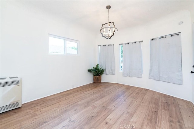 empty room with a chandelier, heating unit, and wood finished floors