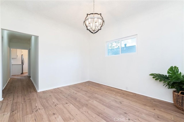 spare room featuring light wood-style floors and an inviting chandelier