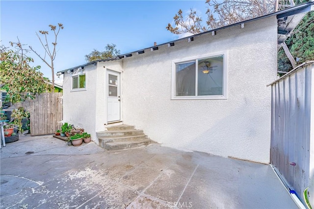 rear view of house with entry steps, a patio area, fence, and stucco siding