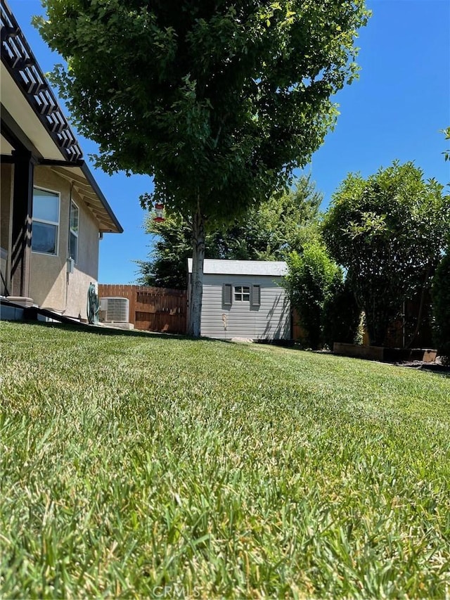 view of yard with a storage unit, an outbuilding, central AC unit, and fence