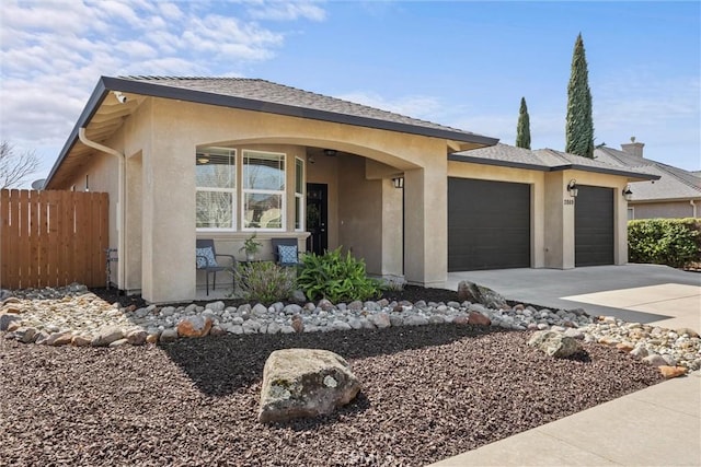 view of front of property featuring stucco siding, driveway, an attached garage, and fence