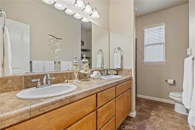 bathroom featuring double vanity, toilet, baseboards, and a sink