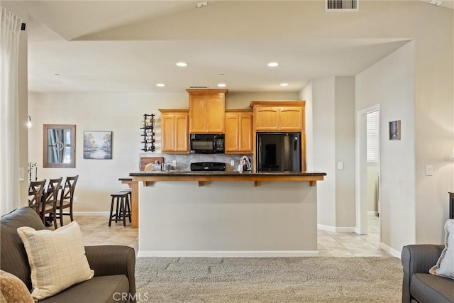 kitchen featuring dark countertops, a breakfast bar, black microwave, fridge, and open floor plan