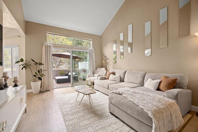 living room with high vaulted ceiling, light wood finished floors, a wealth of natural light, and baseboards